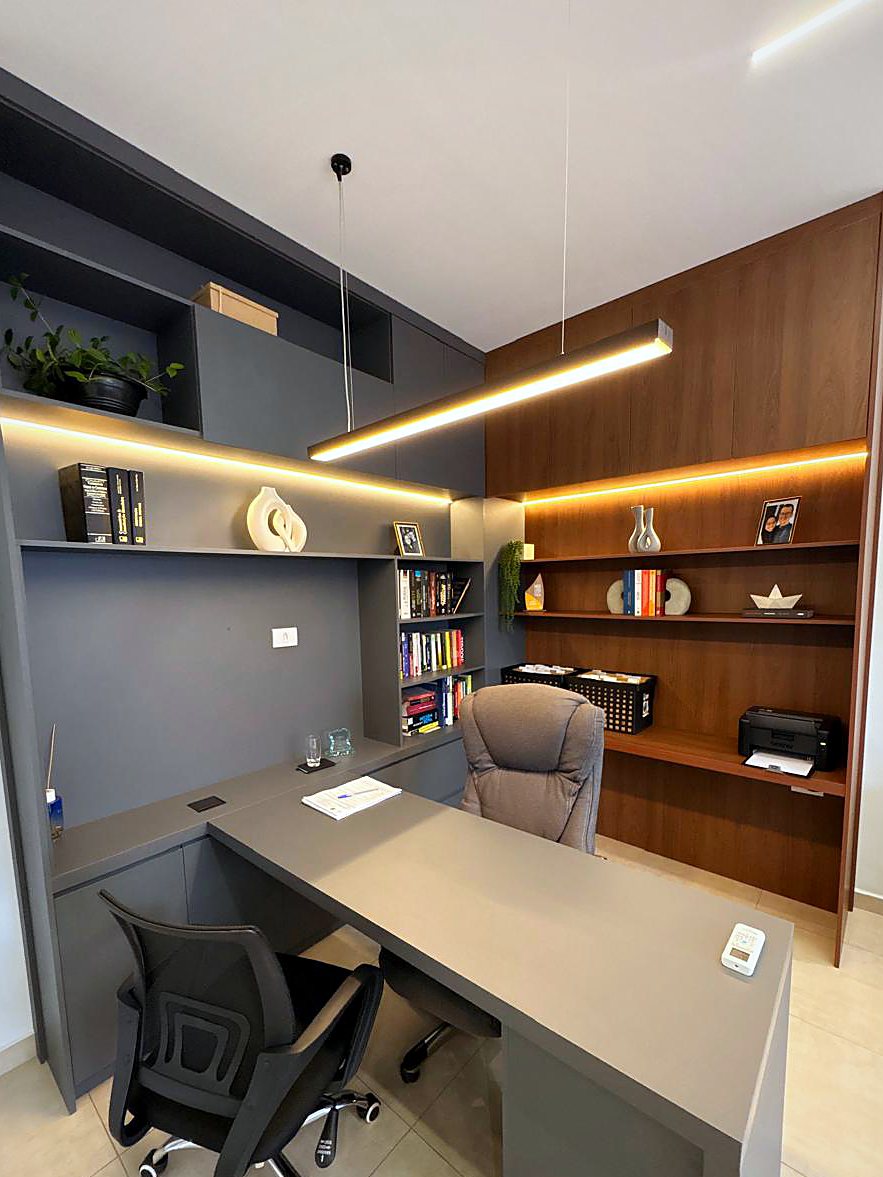 Sala do Dr. Wesley: estantes em madeira e grafite com iluminação embutida, luminária pendente e mesa em L
